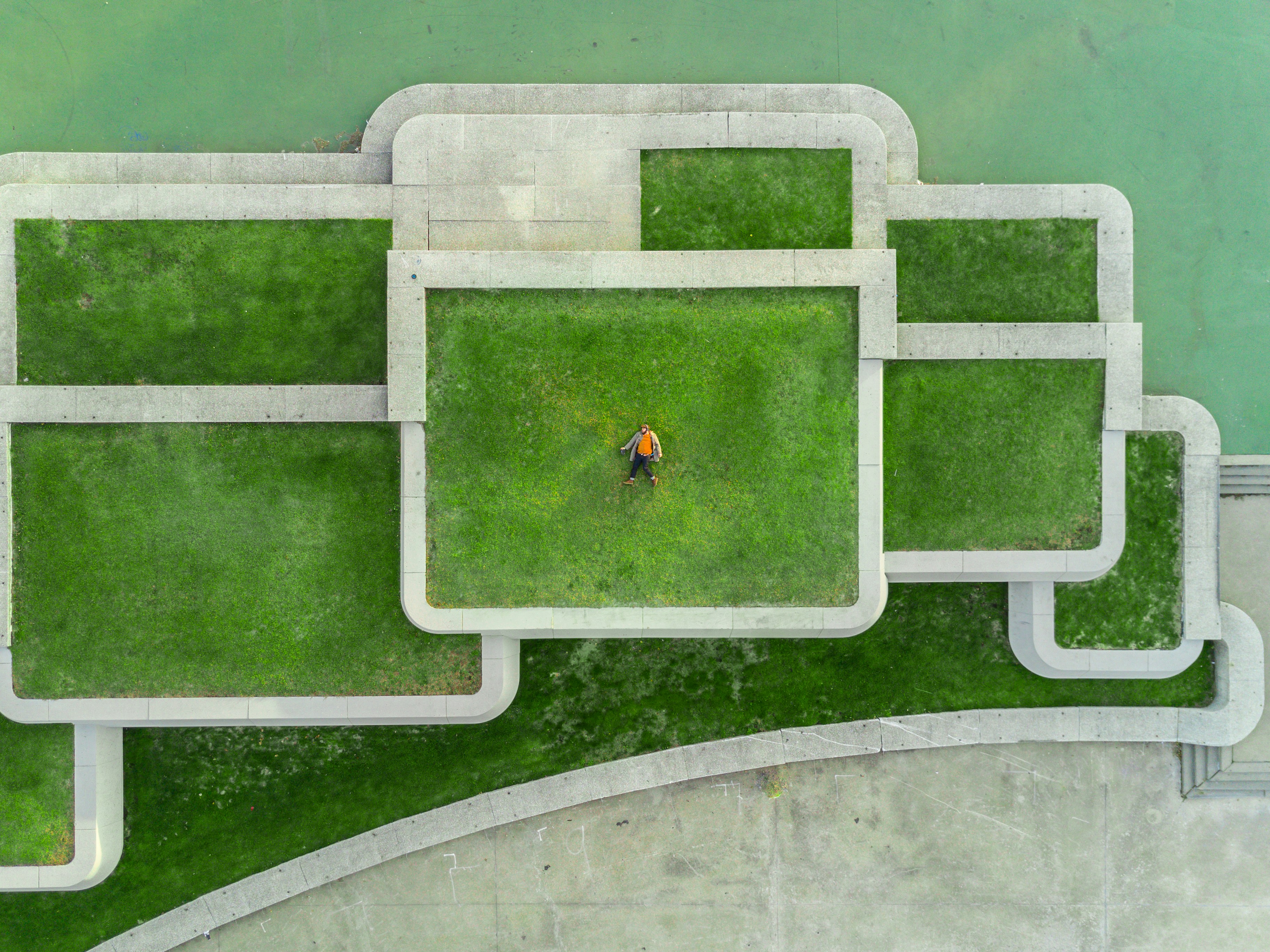 aerial photo of multiple grass areas separated by stone walls. a person lies in the middle area